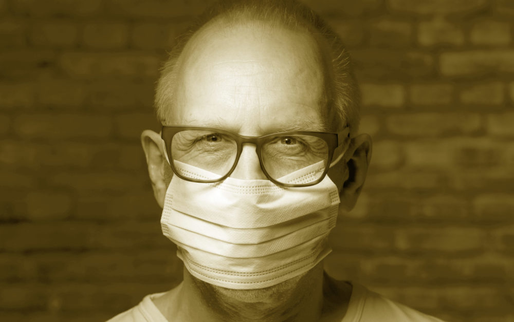 A man wearing a surgical mask in front of a brick wall.